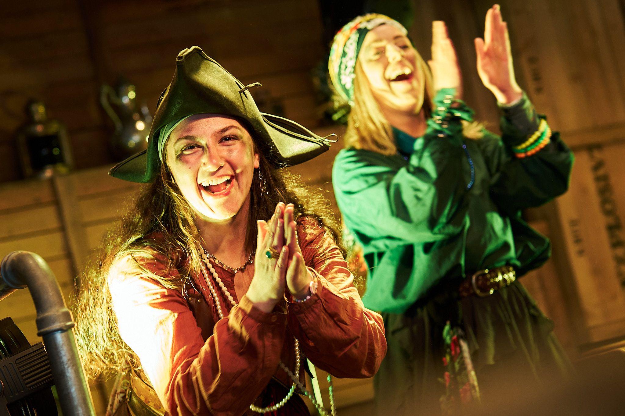 a group of women dressed as pirates are singing into microphones in front of a crowd .